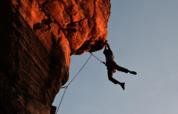 A man rock climbing hanging off of a would at sunset making the rock look red near Happy Acres RV Park in Pueblo CO