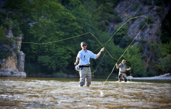 Two men fly fishing in Arkansas River with green trees in the background near Happy Acres RV Park in Pueblo Colorado